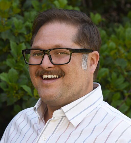 A man with glasses and mustache smiling for the camera.